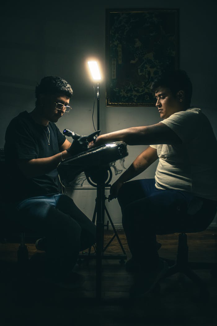 A tattoo artist skillfully creating a design on a client's arm in a softly lit studio setting.