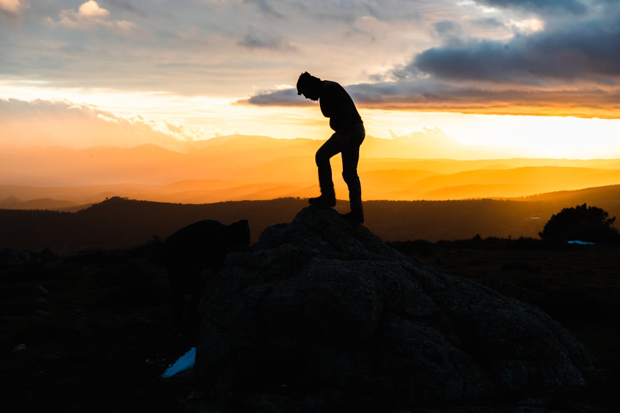 A silhouette of a person on a rock, set against a stunning vibrant sunset with dramatic clouds.